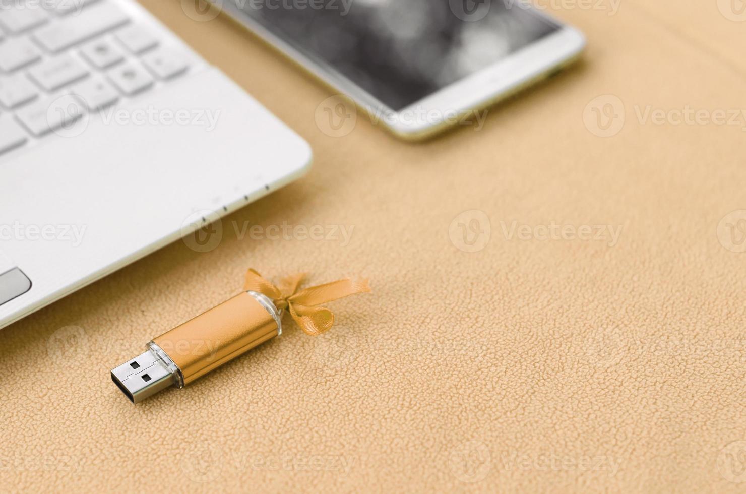 arancia USB veloce memoria carta con un' blu arco bugie su un' coperta di morbido e peloso leggero arancia vello tessuto accanto per un' bianca il computer portatile e smartphone. classico femmina regalo design per un' memoria carta foto