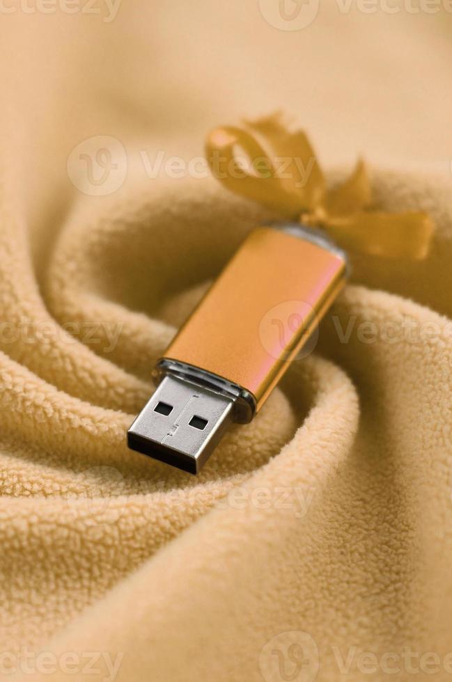 arancia USB veloce memoria carta con un' arco bugie su un' coperta di morbido e peloso leggero arancia vello tessuto con un' lotto di sollievo pieghe. memoria Conservazione dispositivo nel Da donna design foto