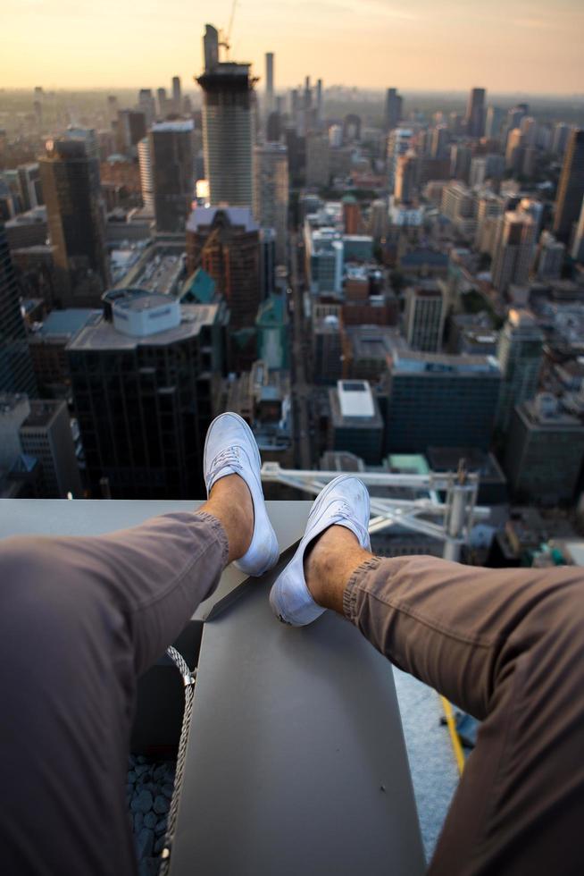 persona seduta in cima a un edificio della città con le gambe tese foto