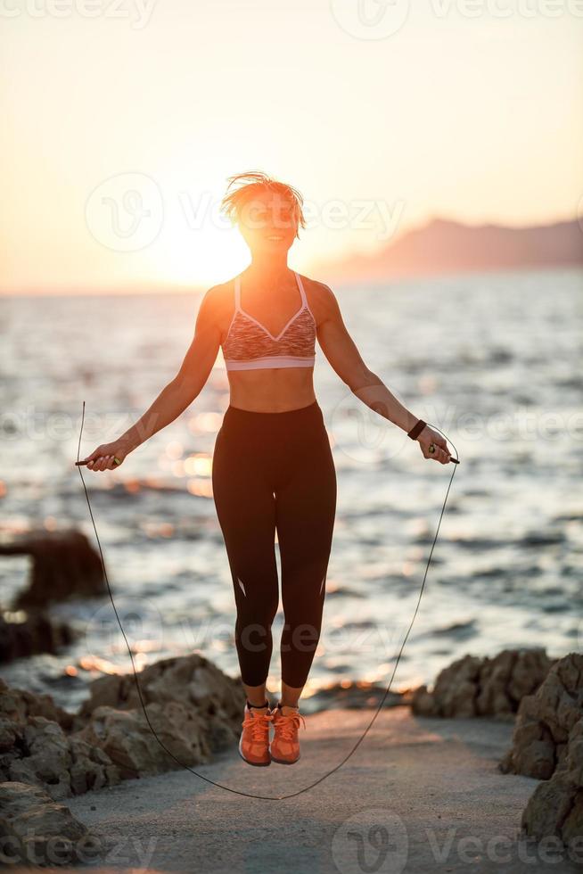 donna salto corda mentre Lavorando su all'aperto formazione vicino il mare foto