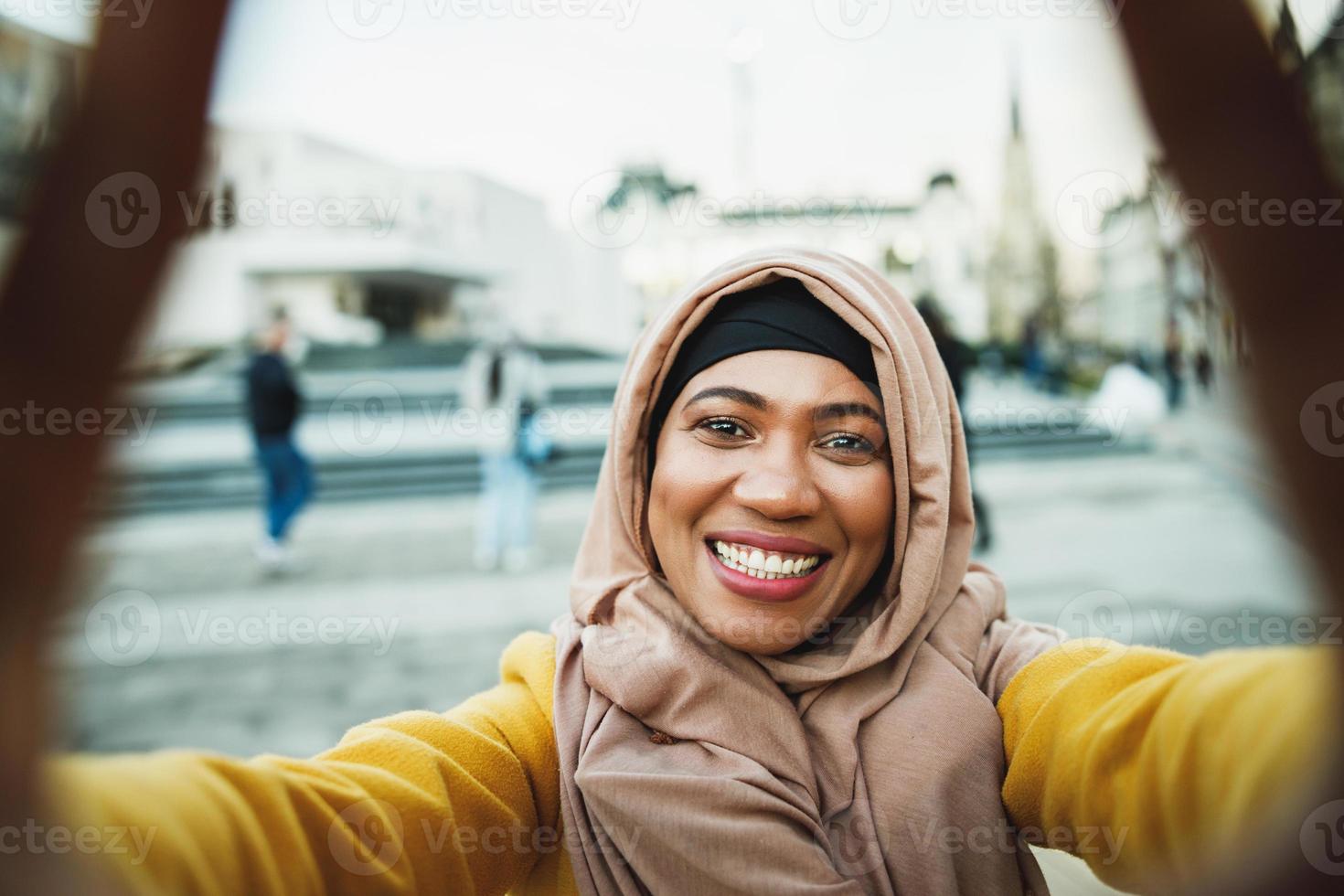 nero musulmano donna con hijab fabbricazione un' autoscatto di inteligente Telefono su il strada foto