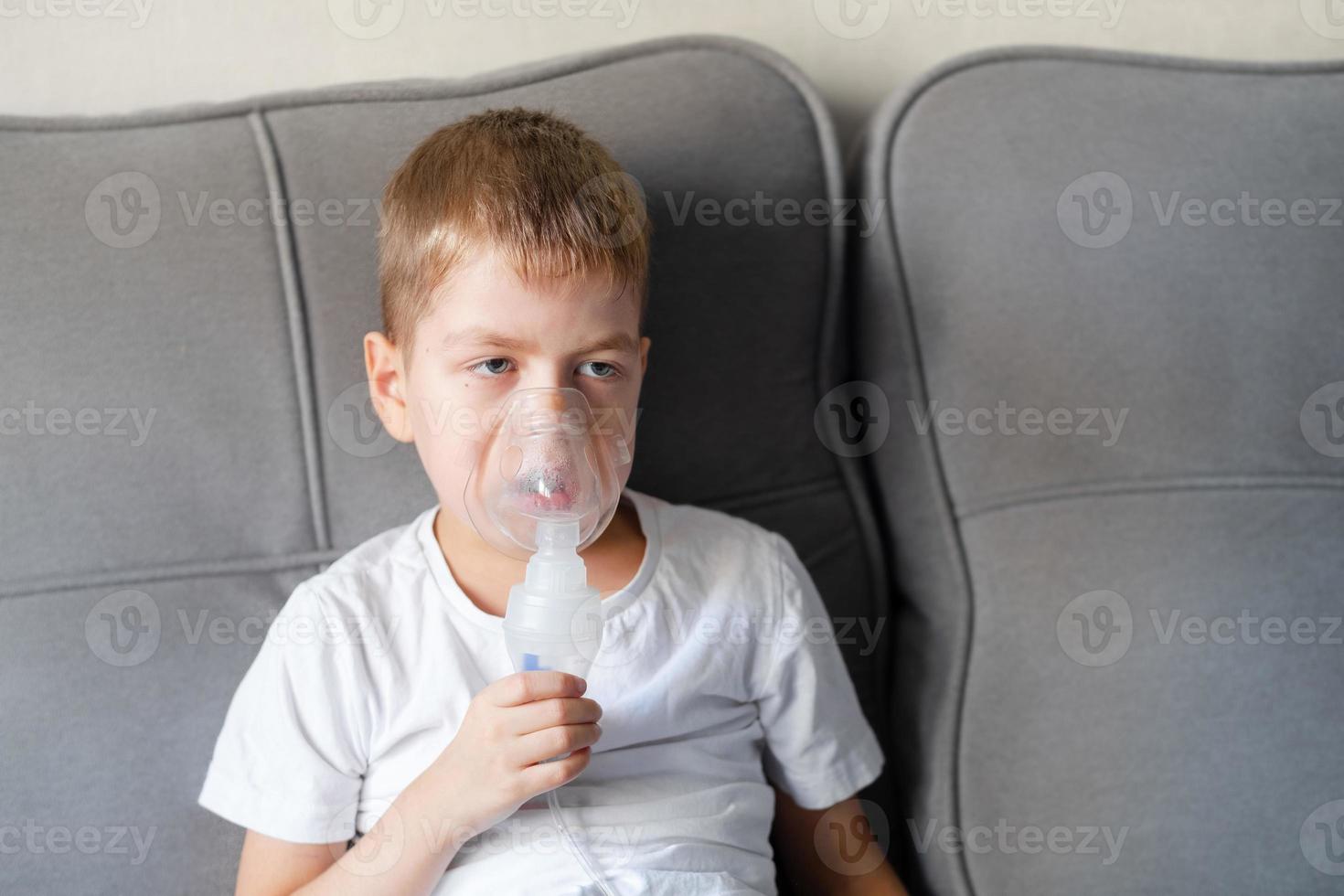 un' poco ragazzo si siede con un inalazione maschera durante tosse e bronchite foto