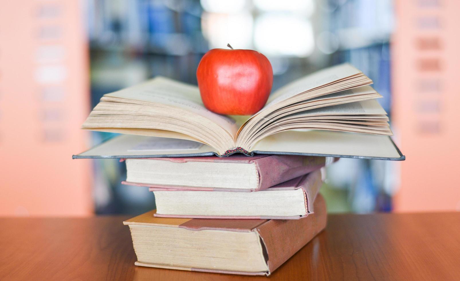 un Mela su il libri su il tavolo con scaffale nel il biblioteca libreria sfondo - formazione scolastica apprendimento concetto Aperto libro pila foto