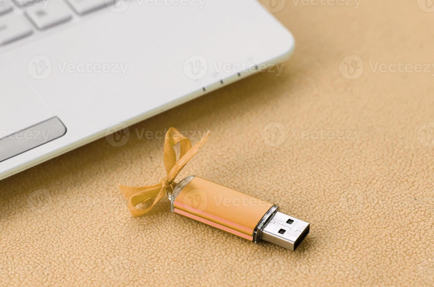 arancia USB veloce memoria carta con un' arco bugie su un' coperta di morbido e peloso leggero arancia vello tessuto accanto per un' bianca il computer portatile. classico femmina regalo design per un' memoria carta foto