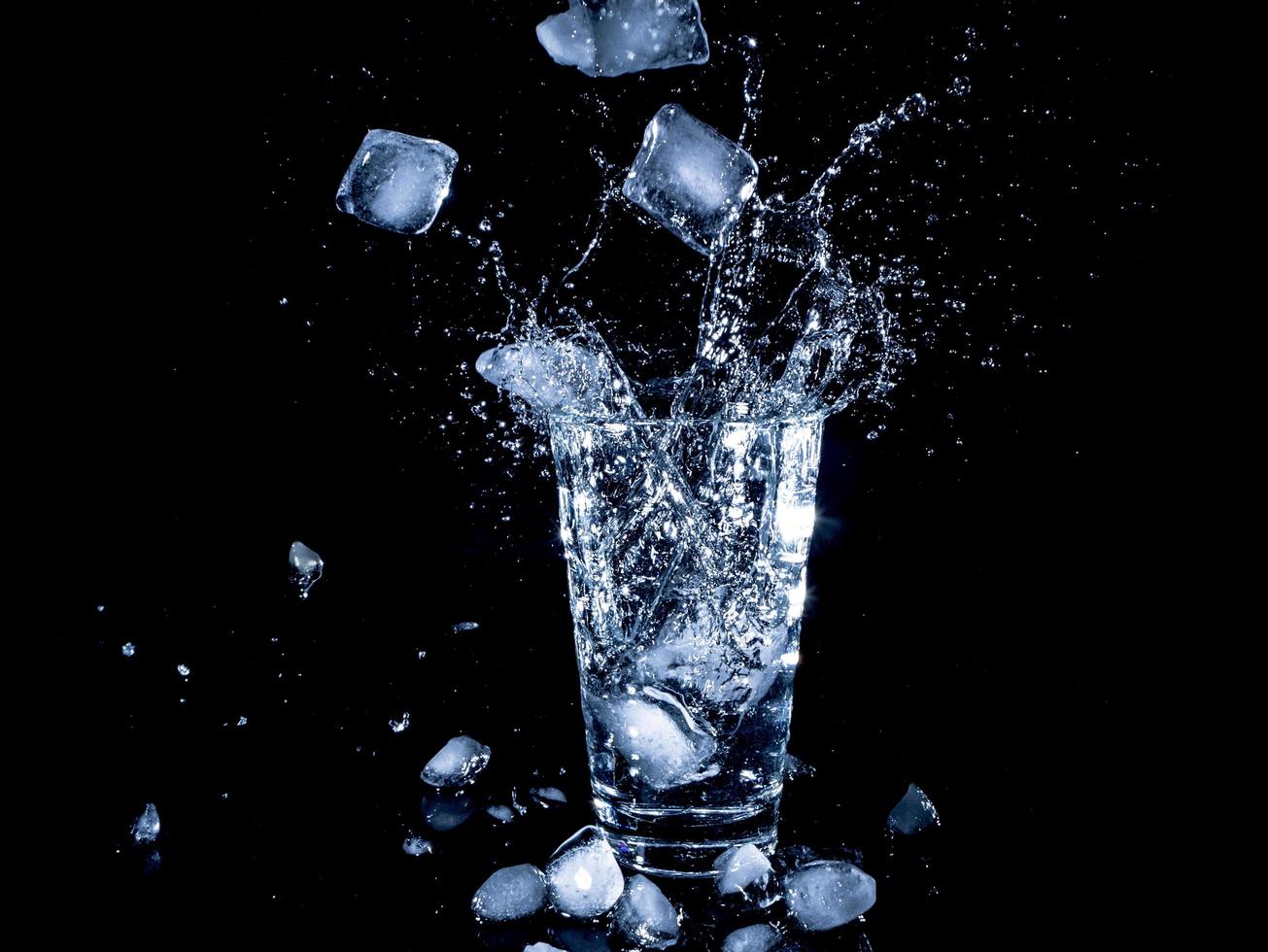 cubetti di ghiaccio caduti in una tazza trasparente con acqua foto