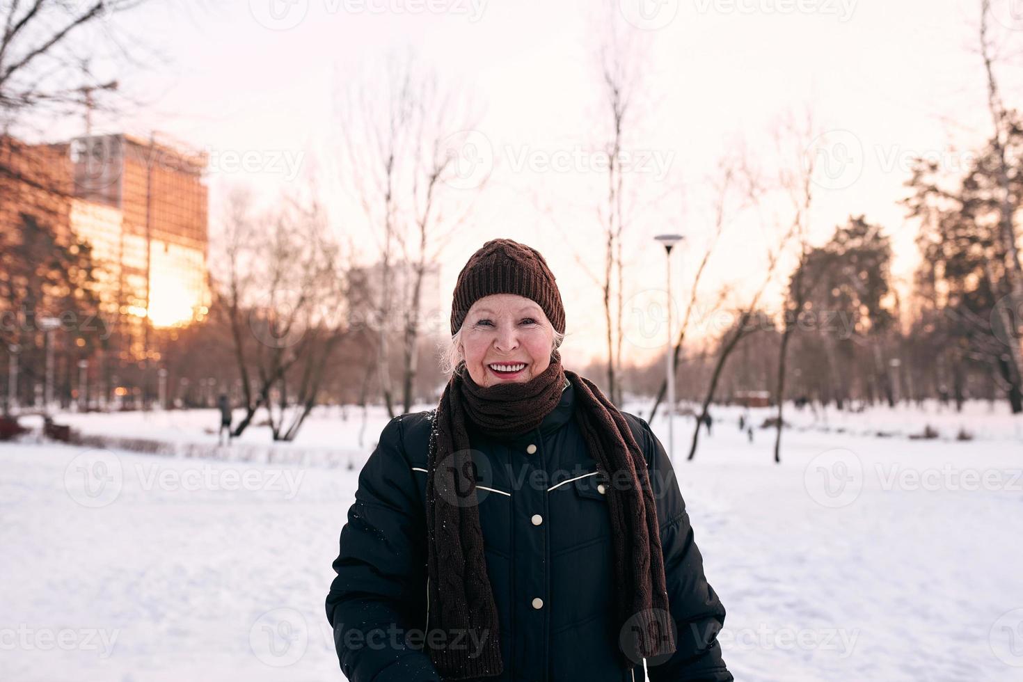 donna anziana in cappello e giacca sportiva che fa valanga nel parco invernale di neve. inverno, età, sport, attività, concetto di stagione foto