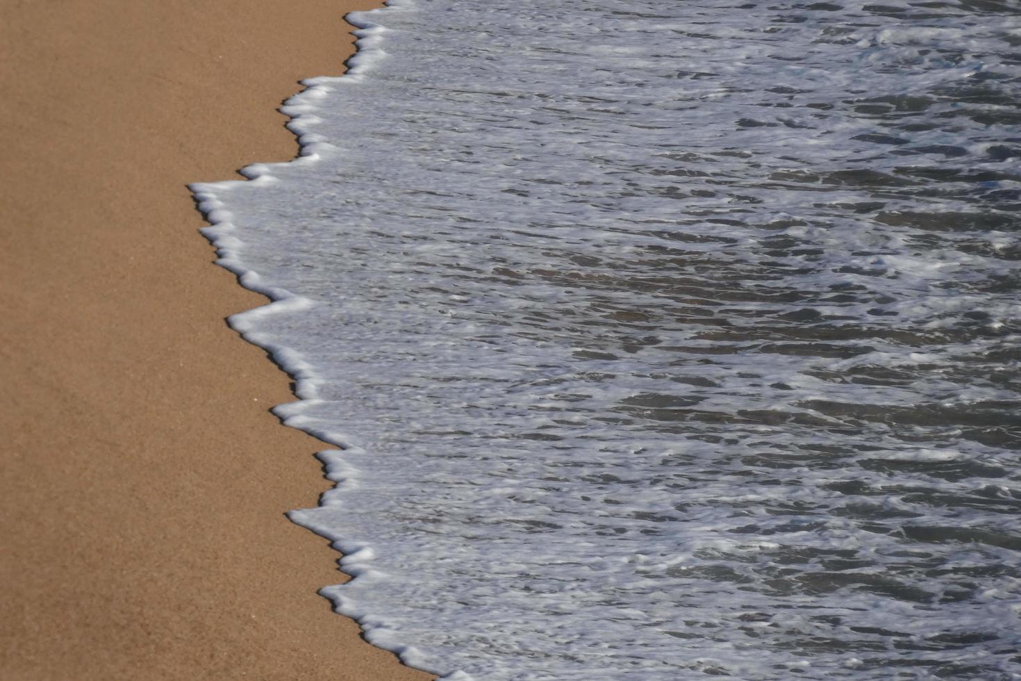 schiuma a partire dal il onde come essi raggiungere il sabbia su il spiaggia foto