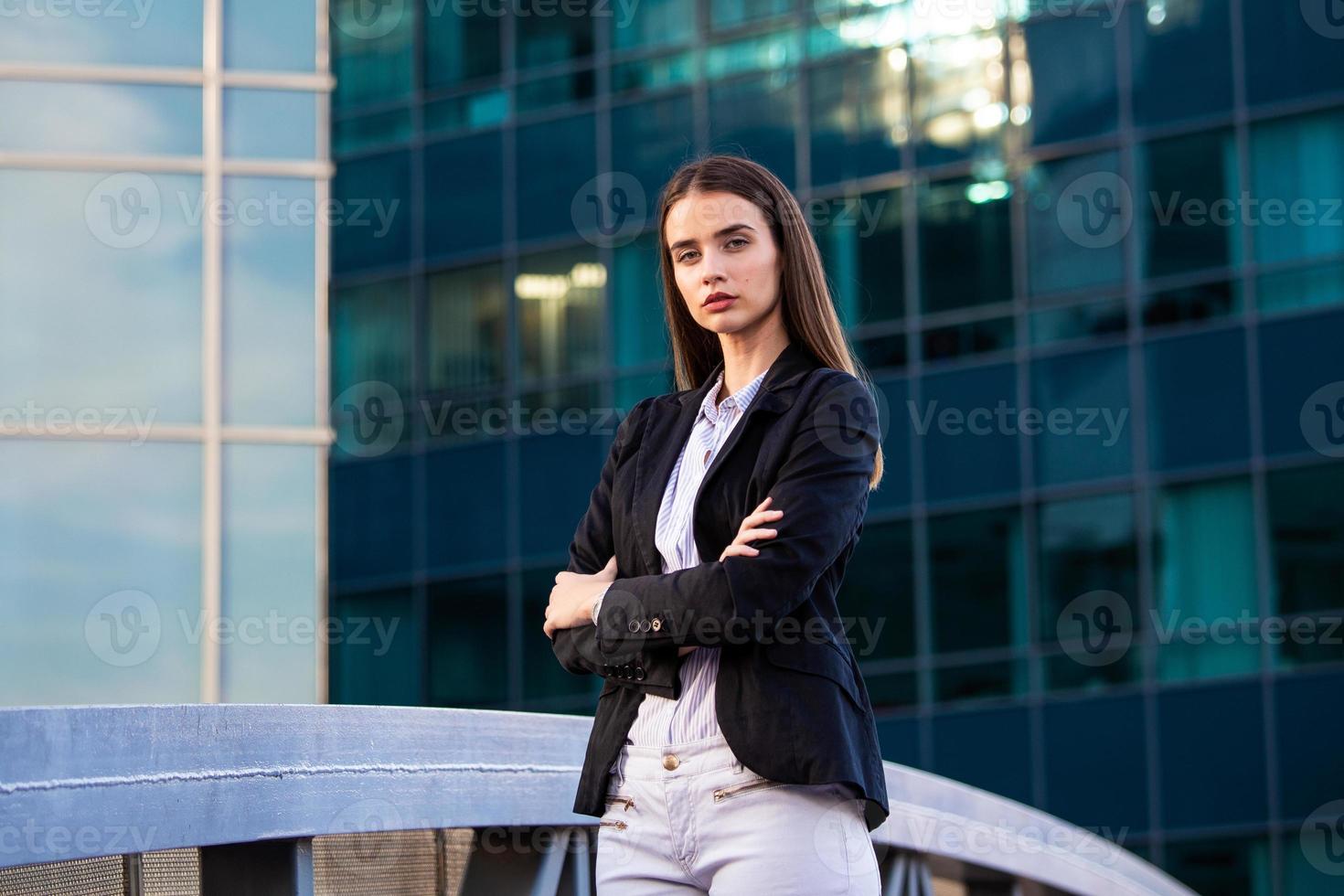 attività commerciale donna con attraversato braccia. fiducioso moderno attività commerciale donna in piedi vicino un' grande finestre neer sua ufficio. foto