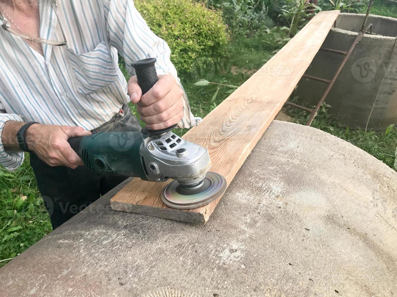 il uomo lavori con il suo mani, macina il disco in giro per il macinino, il elettrico attrezzo per macinazione e lucidatura il superficie di il di legno tavola foto