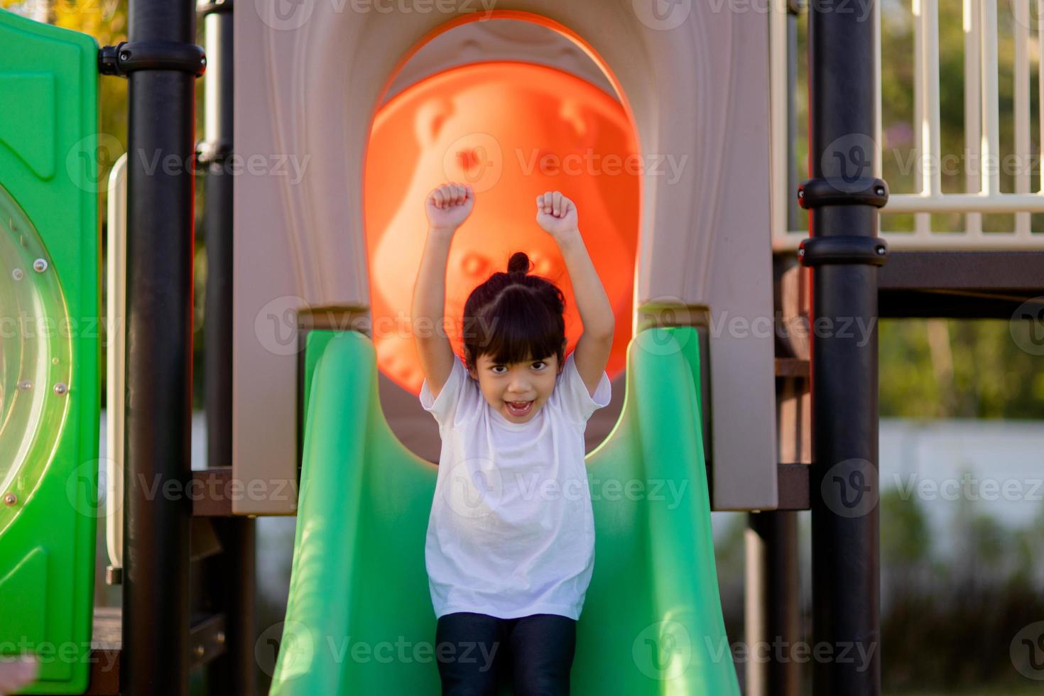 bambino giocando su all'aperto terreno di gioco. bambini giocare su scuola o scuola materna cortile. attivo ragazzo su colorato diapositiva e oscillazione. salutare estate attività per bambini. poco ragazze arrampicata all'aperto. foto