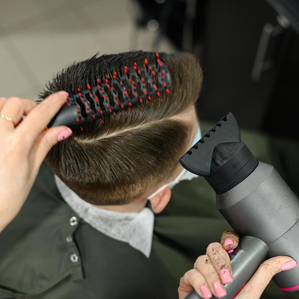 ragazzo adolescente si taglia i capelli durante una pandemia dal barbiere, si taglia i capelli e si asciuga i capelli dopo un taglio di capelli. foto