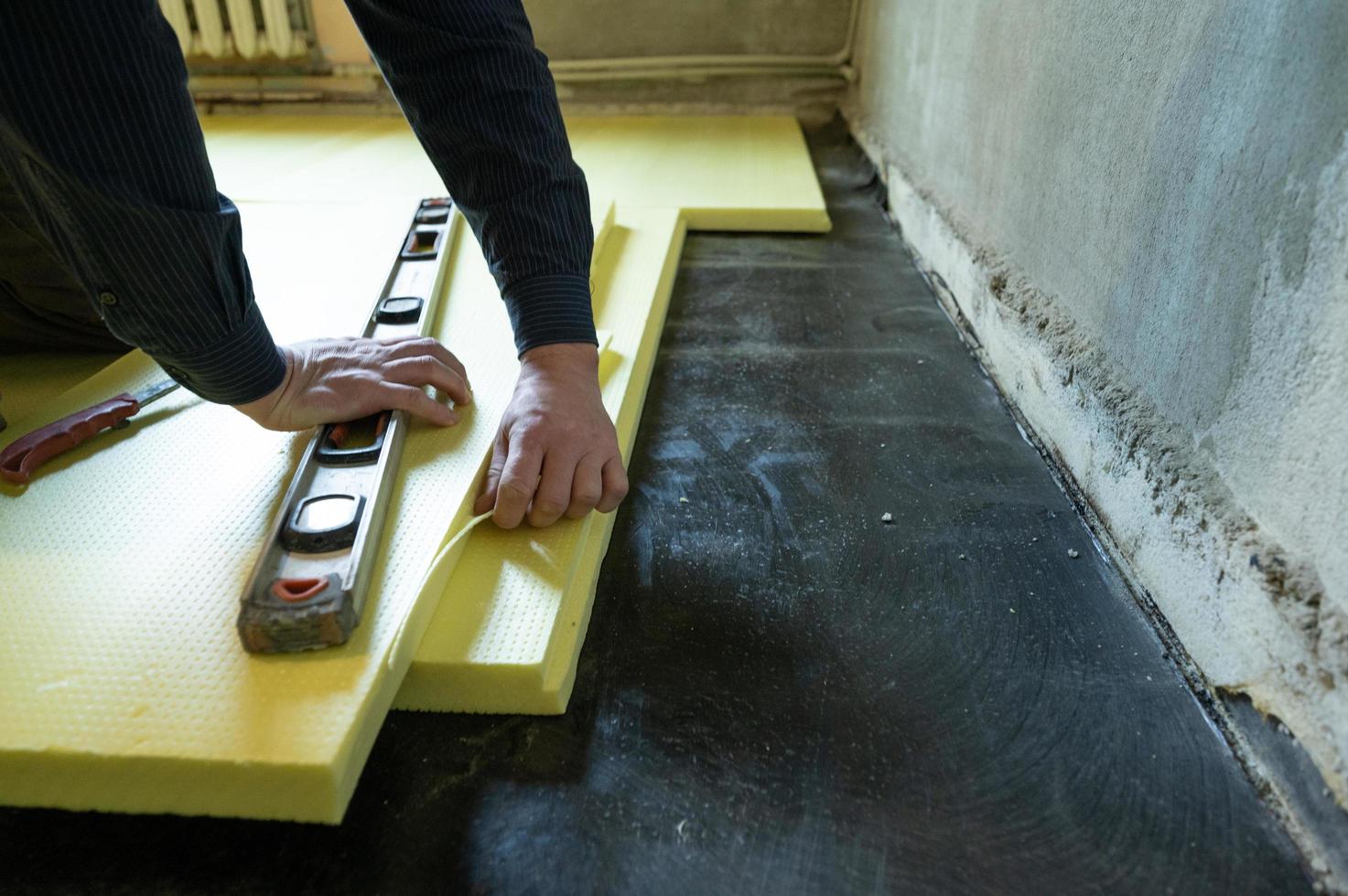 il primo piano del maestro taglia le dimensioni del polistirene espanso sul pavimento, il processo di isolamento del pavimento della casa. foto