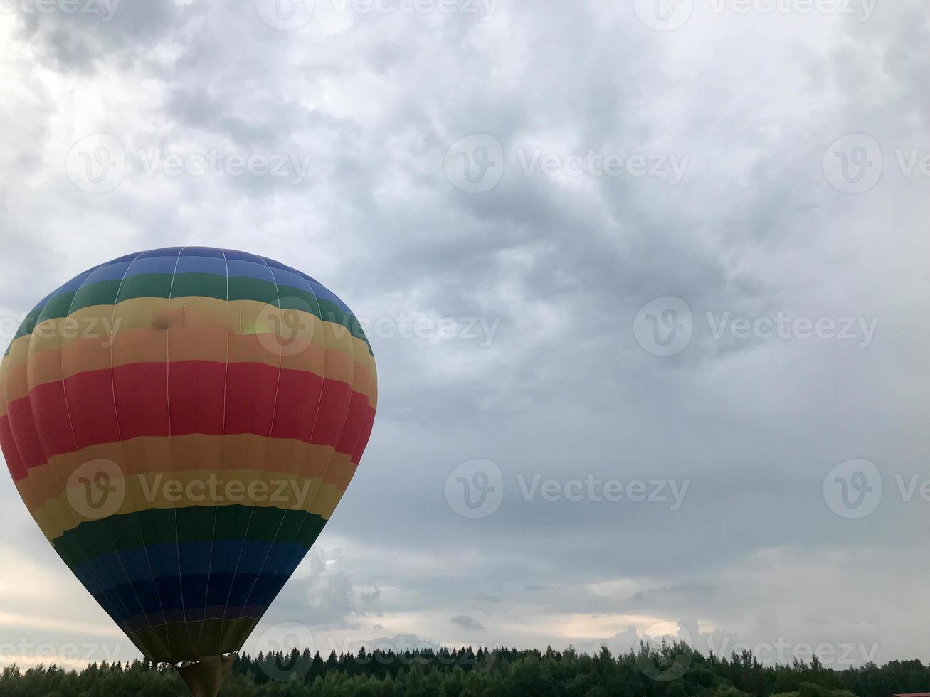 grande multicolore luminosa il giro arcobaleno colorato a strisce a strisce volante Palloncino con un' cestino contro il cielo nel il sera foto