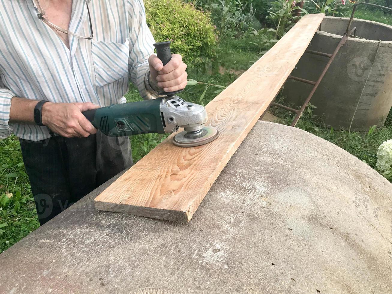 il uomo lavori con il suo mani, macina il disco in giro per il macinino, il elettrico attrezzo per macinazione e lucidatura il superficie di il di legno tavola foto