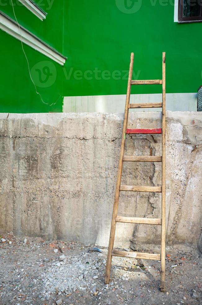 di legno scala è appoggiato su contro un' alto calcestruzzo portico, quale è fatiscente, contro il fondale di il edificio verde parete. foto