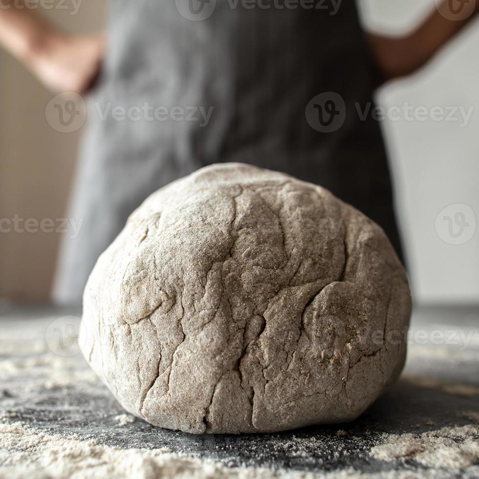 Impasto bugie su un' tavolo cosparso con Farina, un' panettiere sta contro un' sfocato sfondo e detiene pugni su il suo fianchi. pane fabbricazione. foto