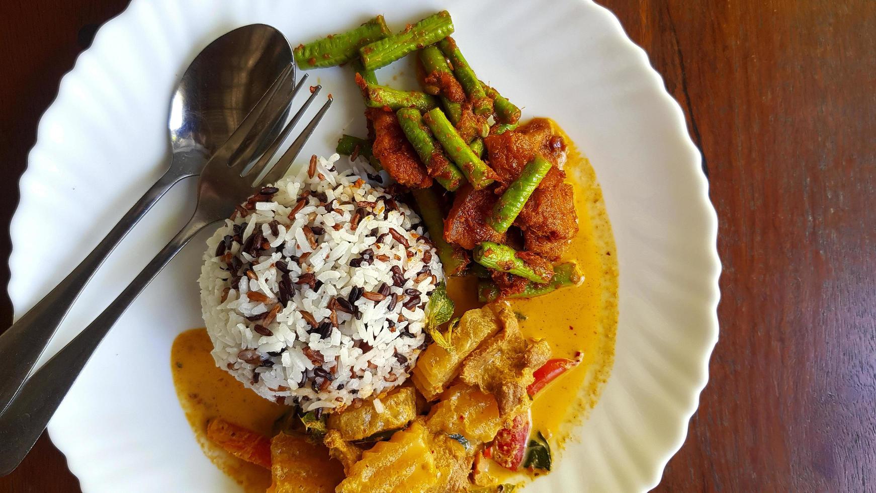 superiore Visualizza di tre colore riso con speziato giallo curry con Maiale e agitare fritte Maiale pancia e rosso curry incolla con corda fagiolo nel bianca piatto su Marrone di legno sfondo o tavolo con copia spazio. foto