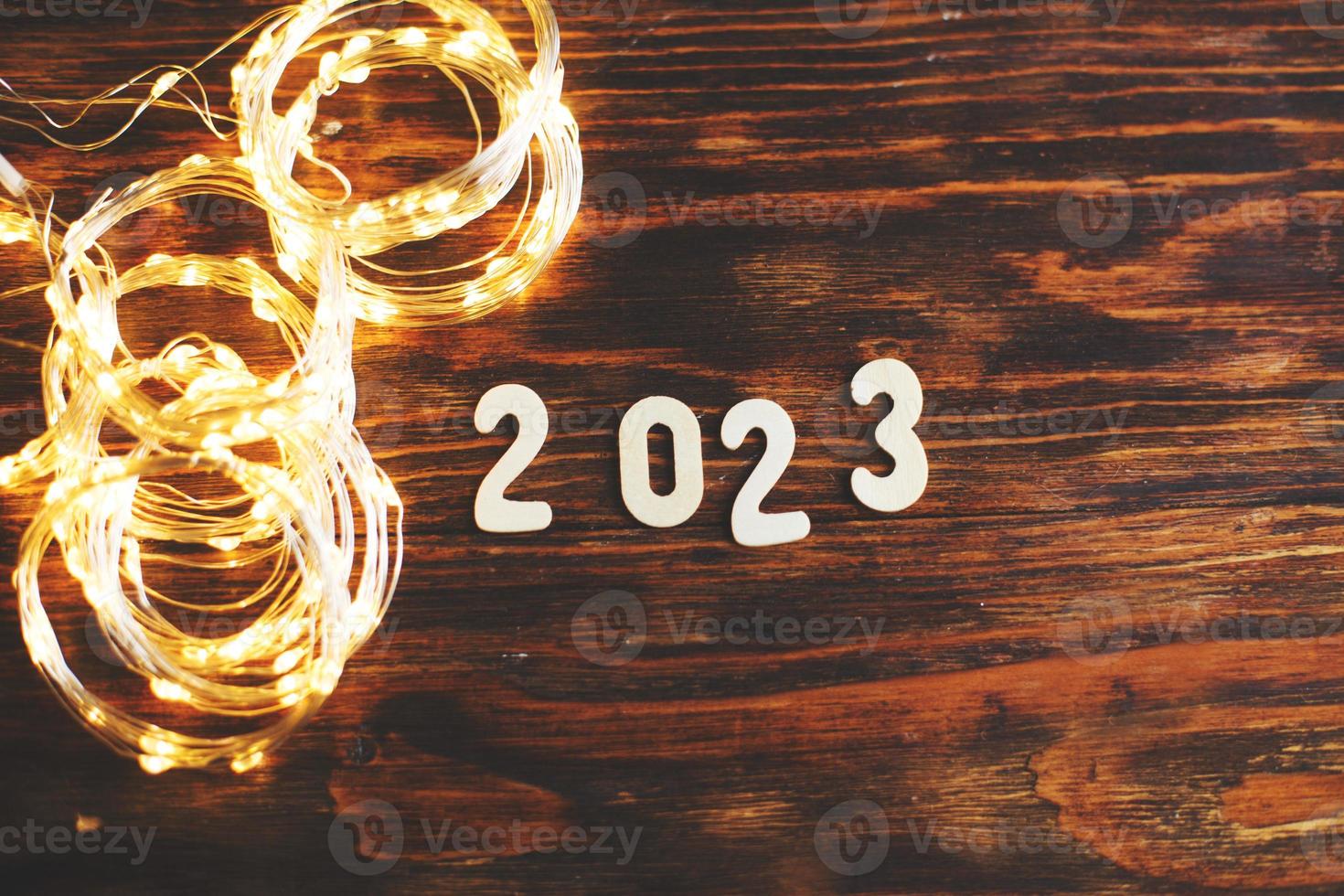 di legno numero 2023 su Natale brillante di legno sfondo. con scintillare festivo oro ghirlanda foto