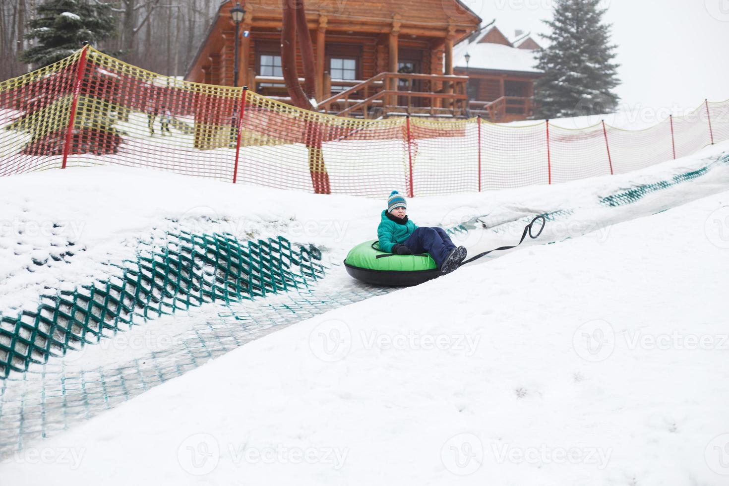 bambino avendo divertimento su neve tubo. ragazzo è equitazione un' tubo. inverno intrattenimento. ragazzo scorrevole discesa su tubo foto