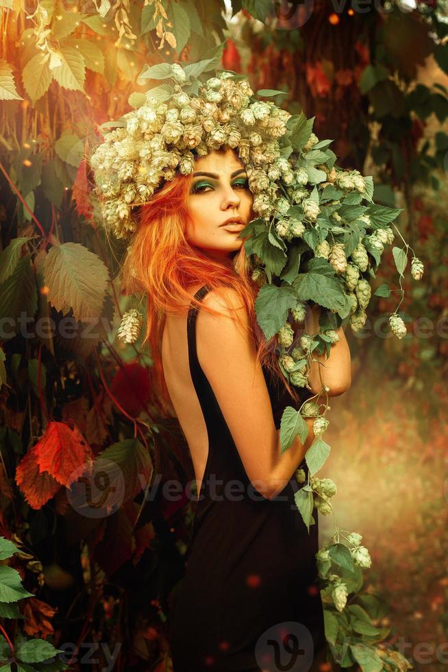 sensuale ritratto di giovane redheair signora con ghirlanda di luppolo su testa nel Magia foresta foto