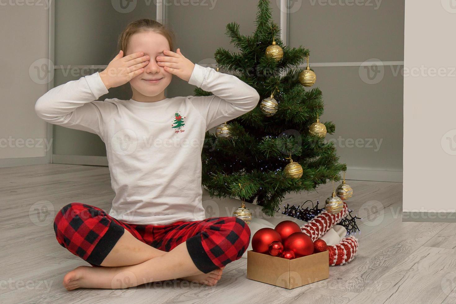 ragazza nel pigiama chiuso sua occhi seduta di il Natale albero, inverno vacanze foto