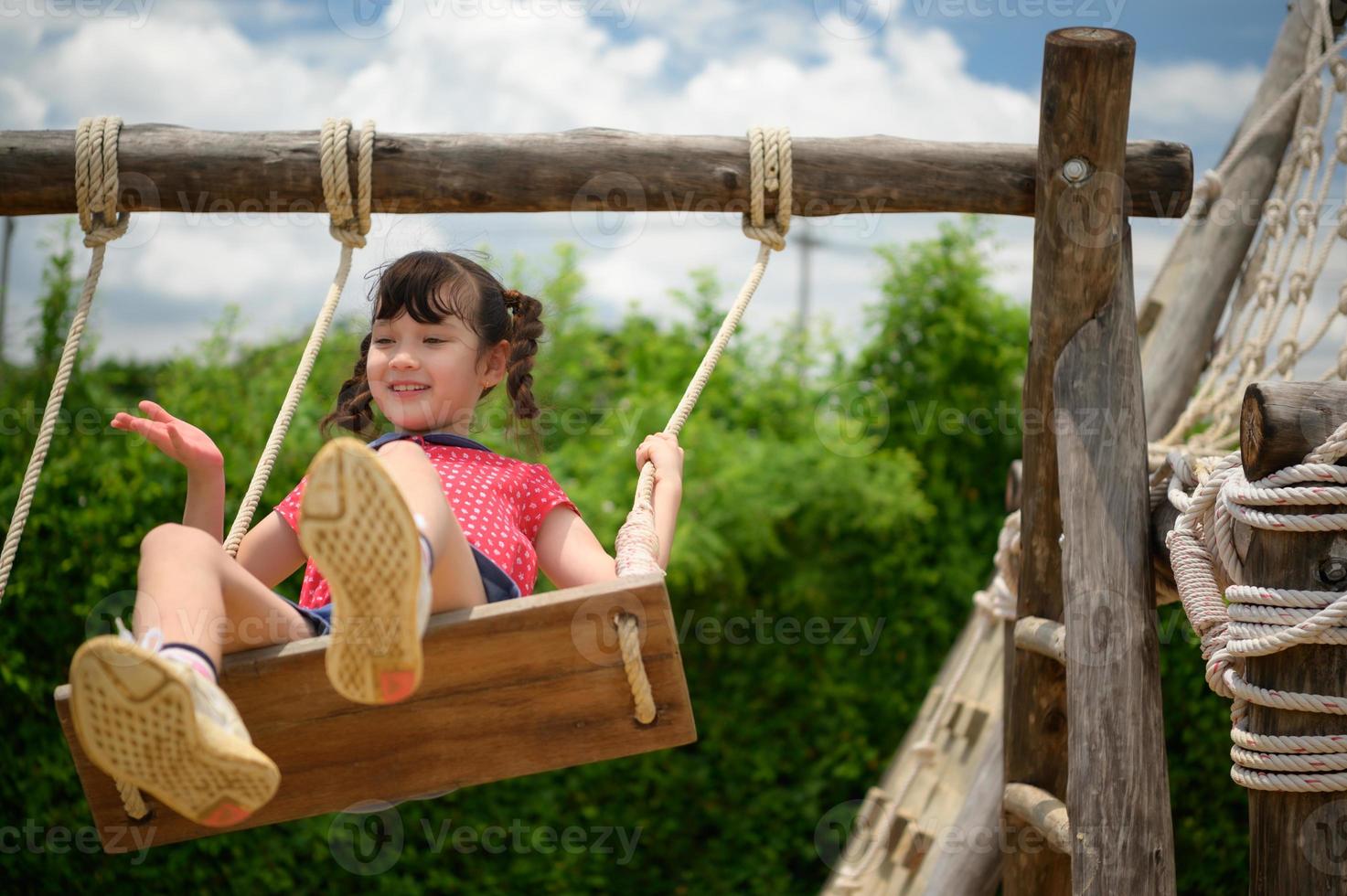 un' poco ragazza avendo divertimento oscillante su un' swing su un' chiaro giorno foto