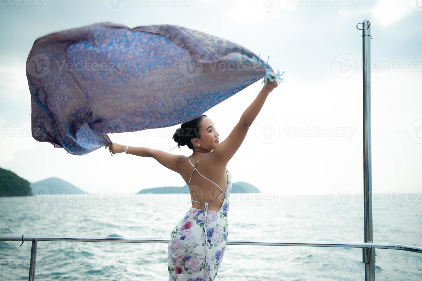 un asiatico ragazza su un' yacht In piedi per ricevere il fresco aria a partire dal il mare con un' scialle quello volò nel bellissimo onde foto