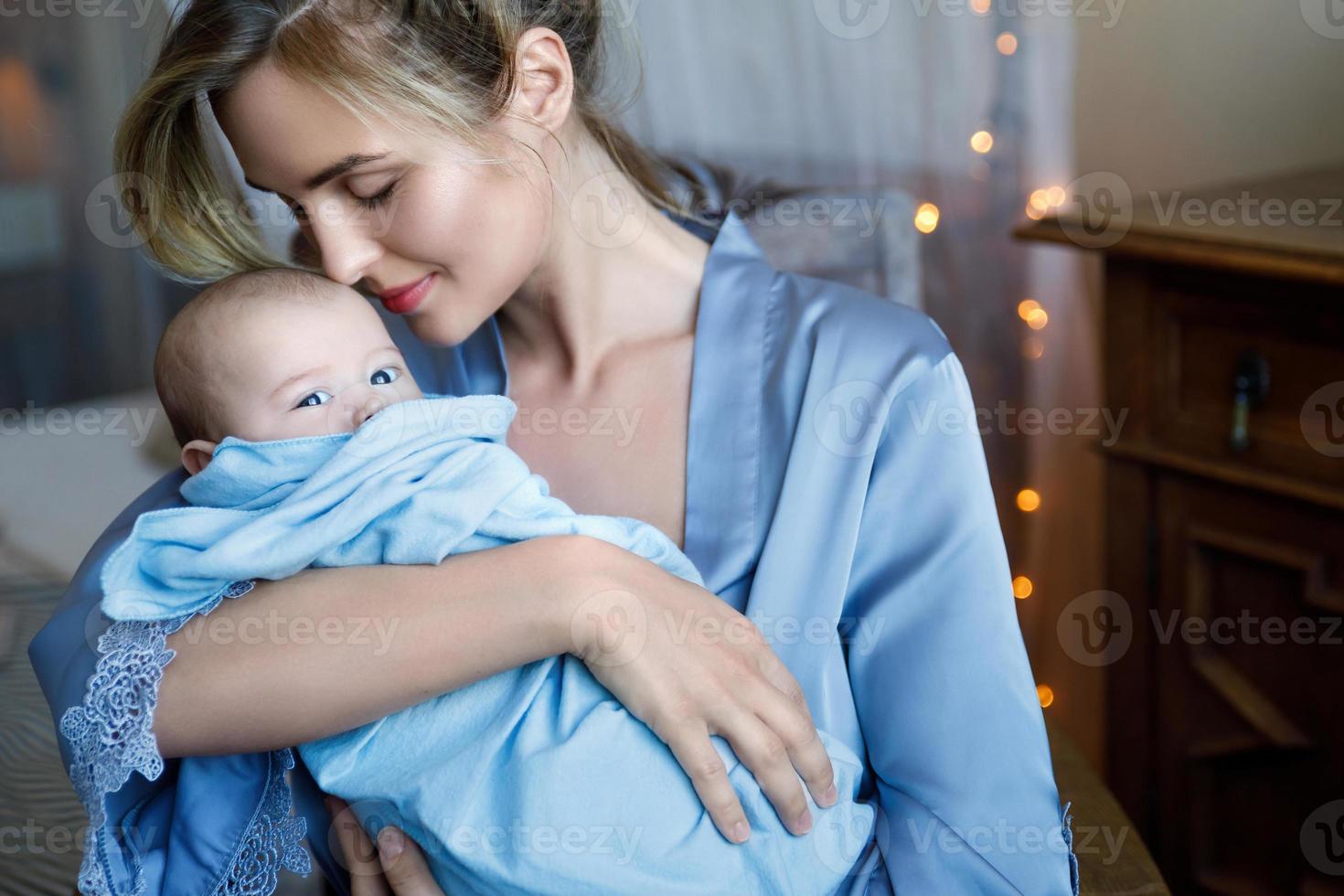 giovane bellissimo madre con sua carino poco bambino avvolto nel il blu stoffa foto