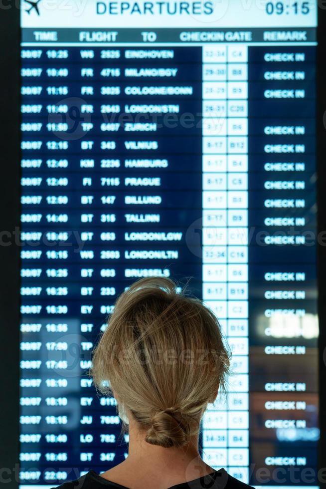 donna guardare su il Schermo con informazione di un' voli nel un aeroporto foto