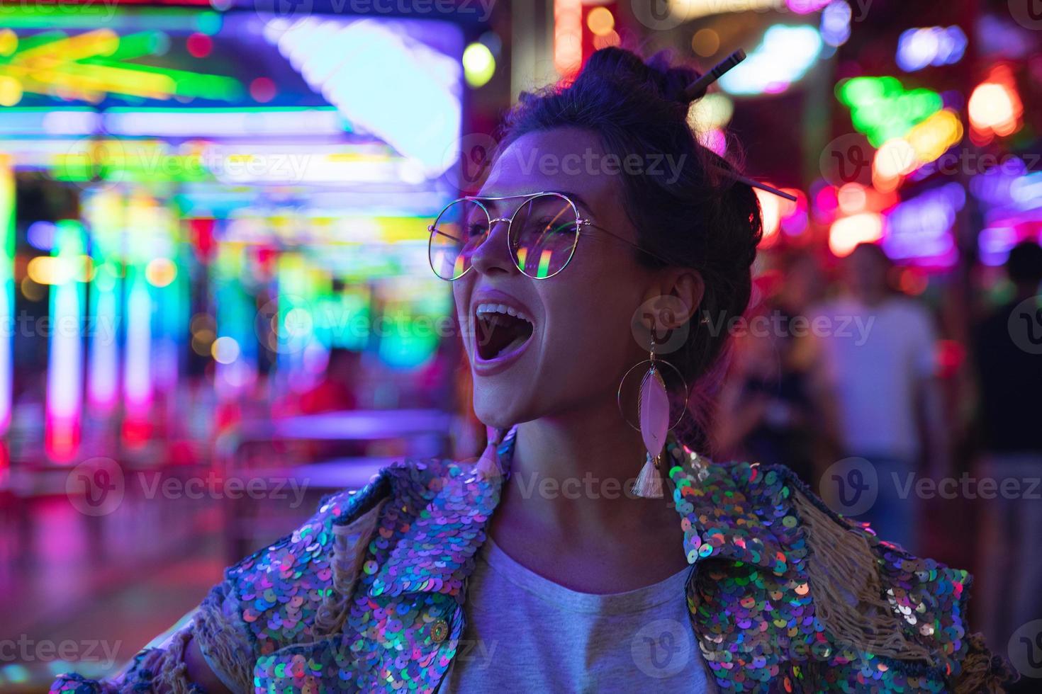 elegante donna indossare giacca con splendente paillettes su il città strada con neon luci foto