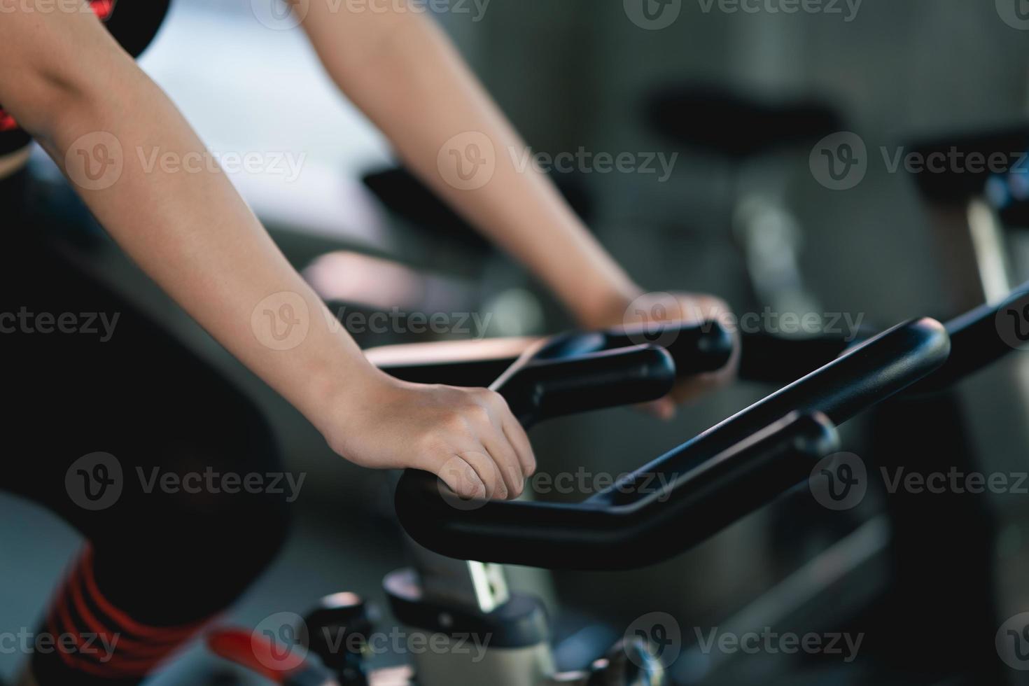 Ritaglia immagine di vicino su mano sportiva esercizio su un' bicicletta nel il palestra, determinazione per cardio perdere il peso, fa sua sano. esercizio bicicletta donna fitness sport concetto. foto