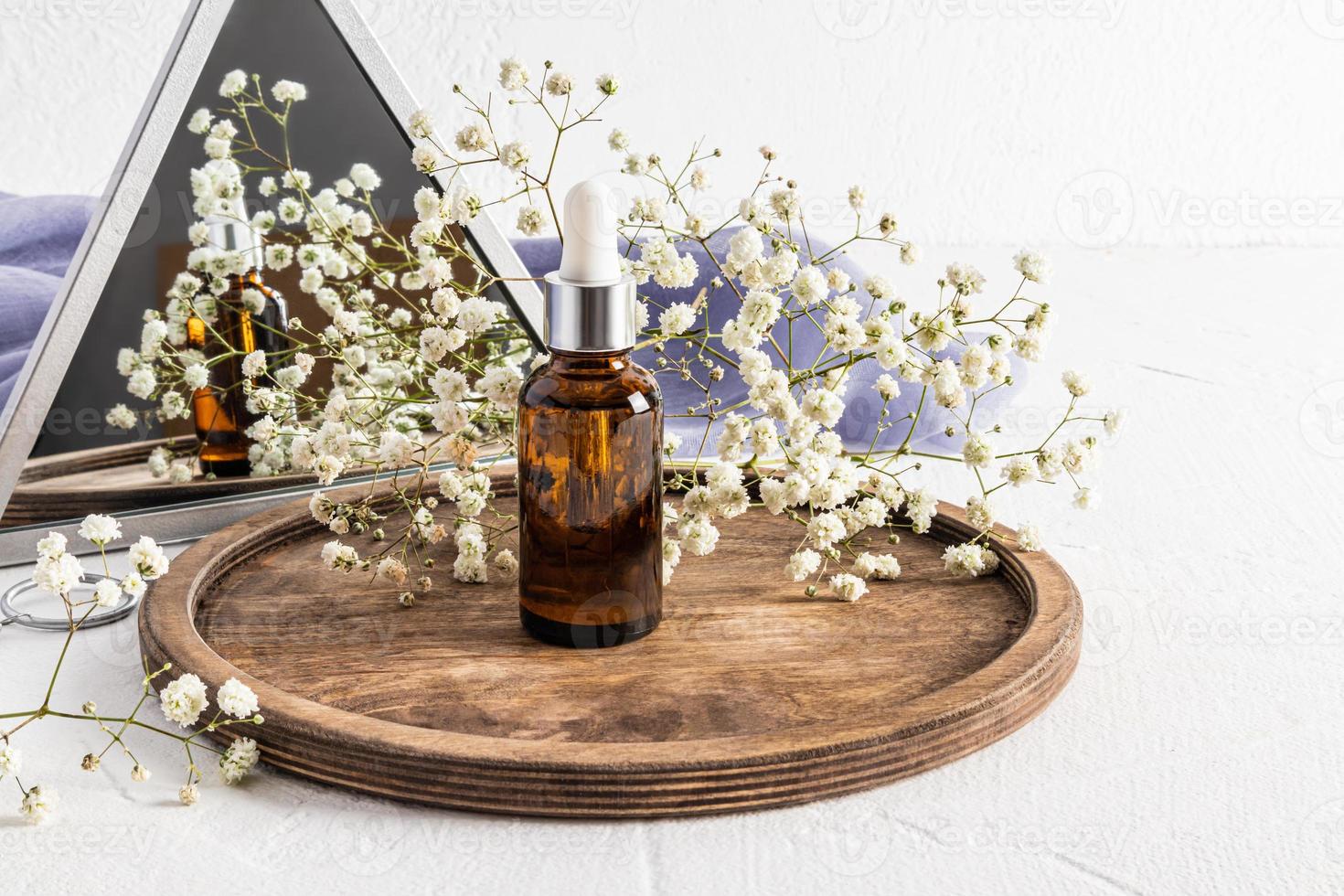 facciale pelle cura siero nel un' bicchiere bottiglia con un' contagocce sta su un' di legno il giro vassoio con un' gypsophila a il specchio. naturale cosmetici. foto