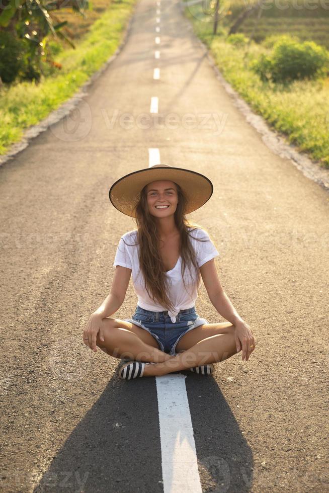 contento donna è seduta nel il mezzo di il asfalto strada foto