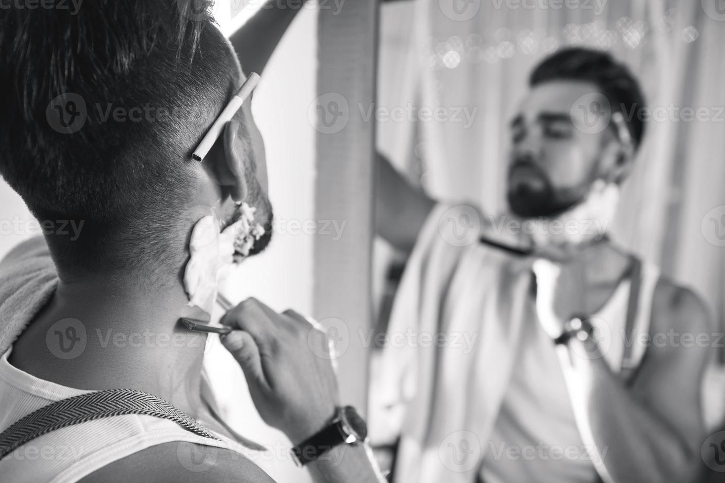 uomo guardare nel il specchio e rasatura il suo barba con un' dritto rasoio foto