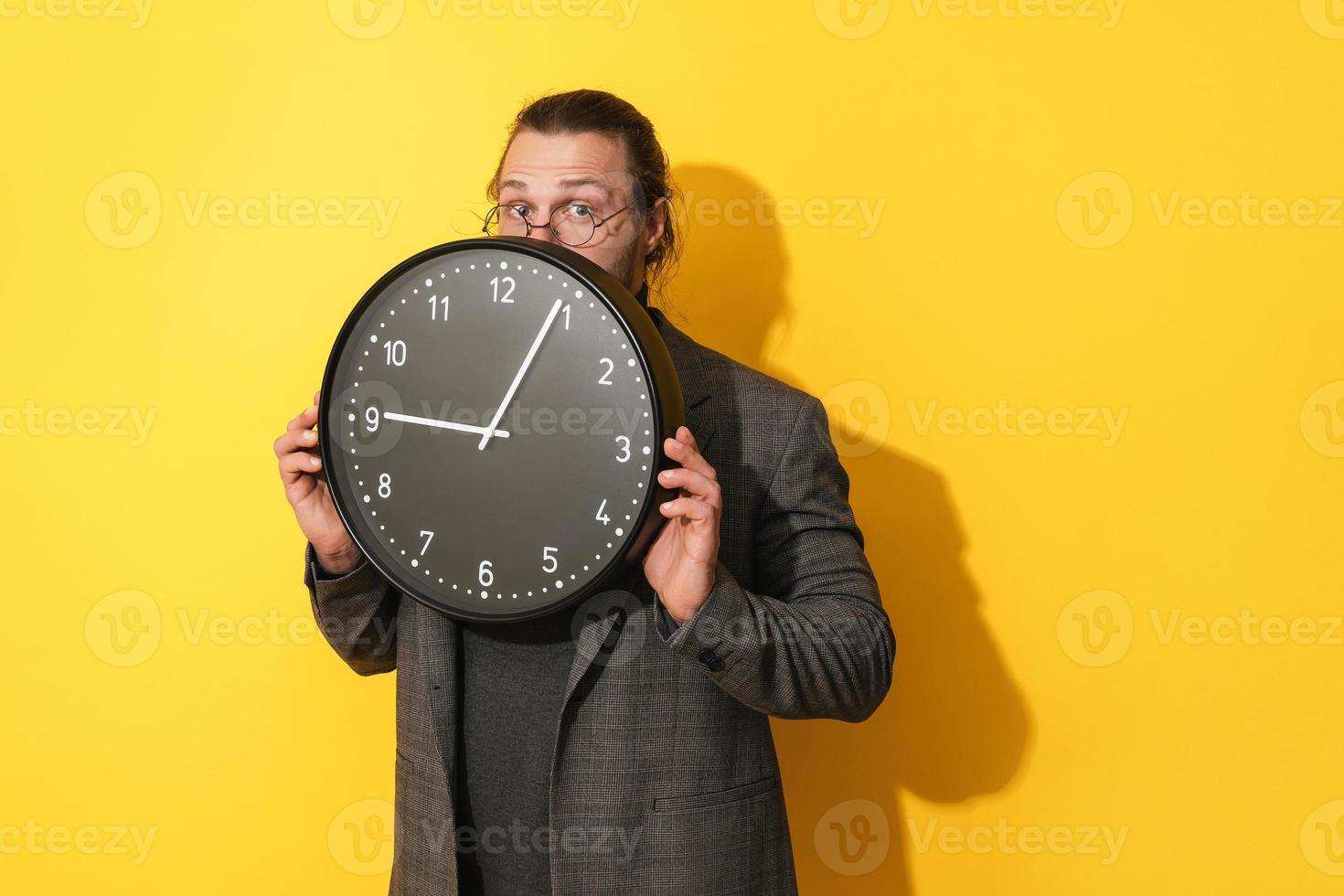 giovane uomo sbirciando su a partire dal dietro a grande orologio su un' giallo sfondo foto