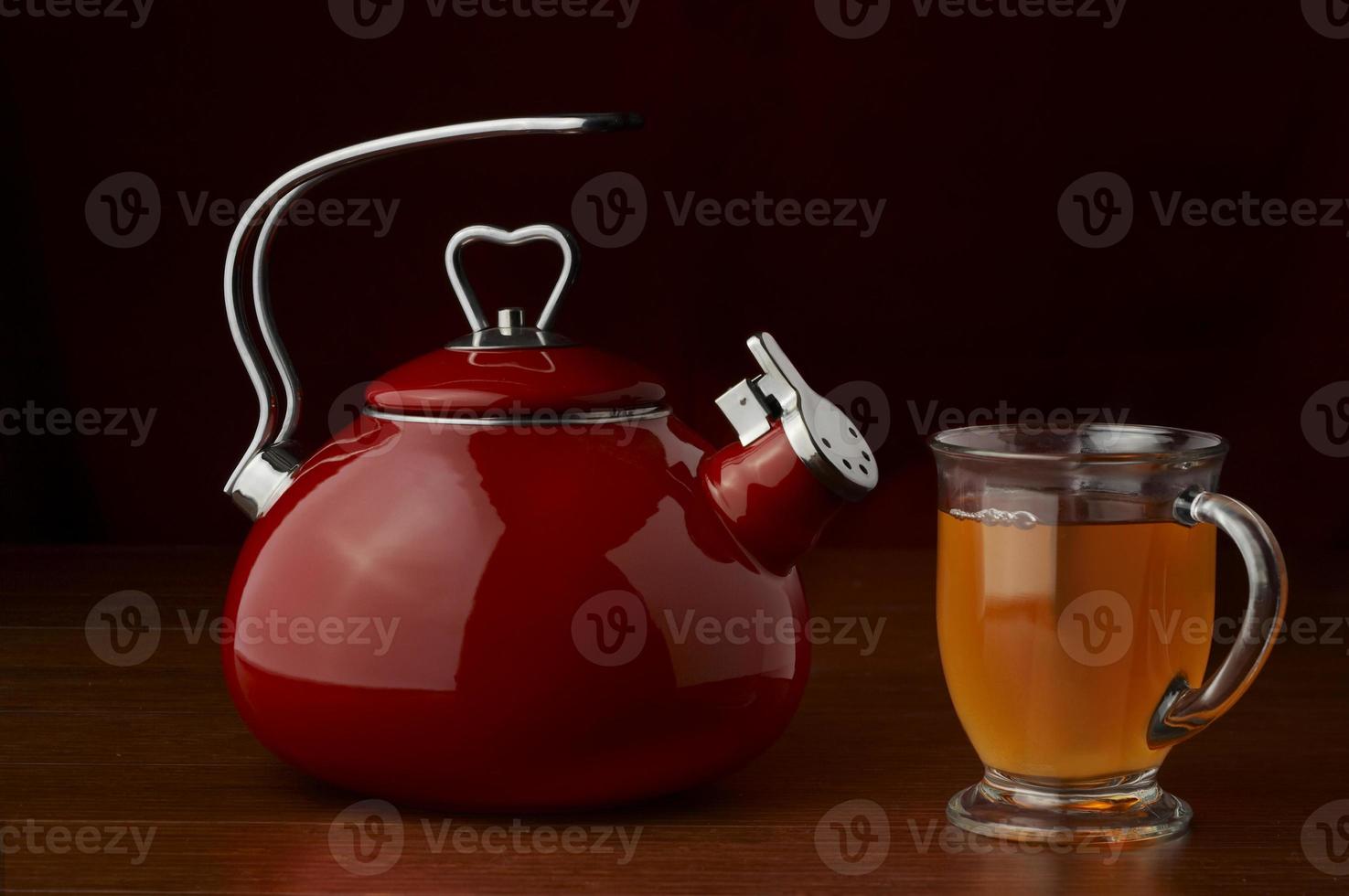 un' rosso bollitore su un' buio sfondo con un' tazza di tè foto