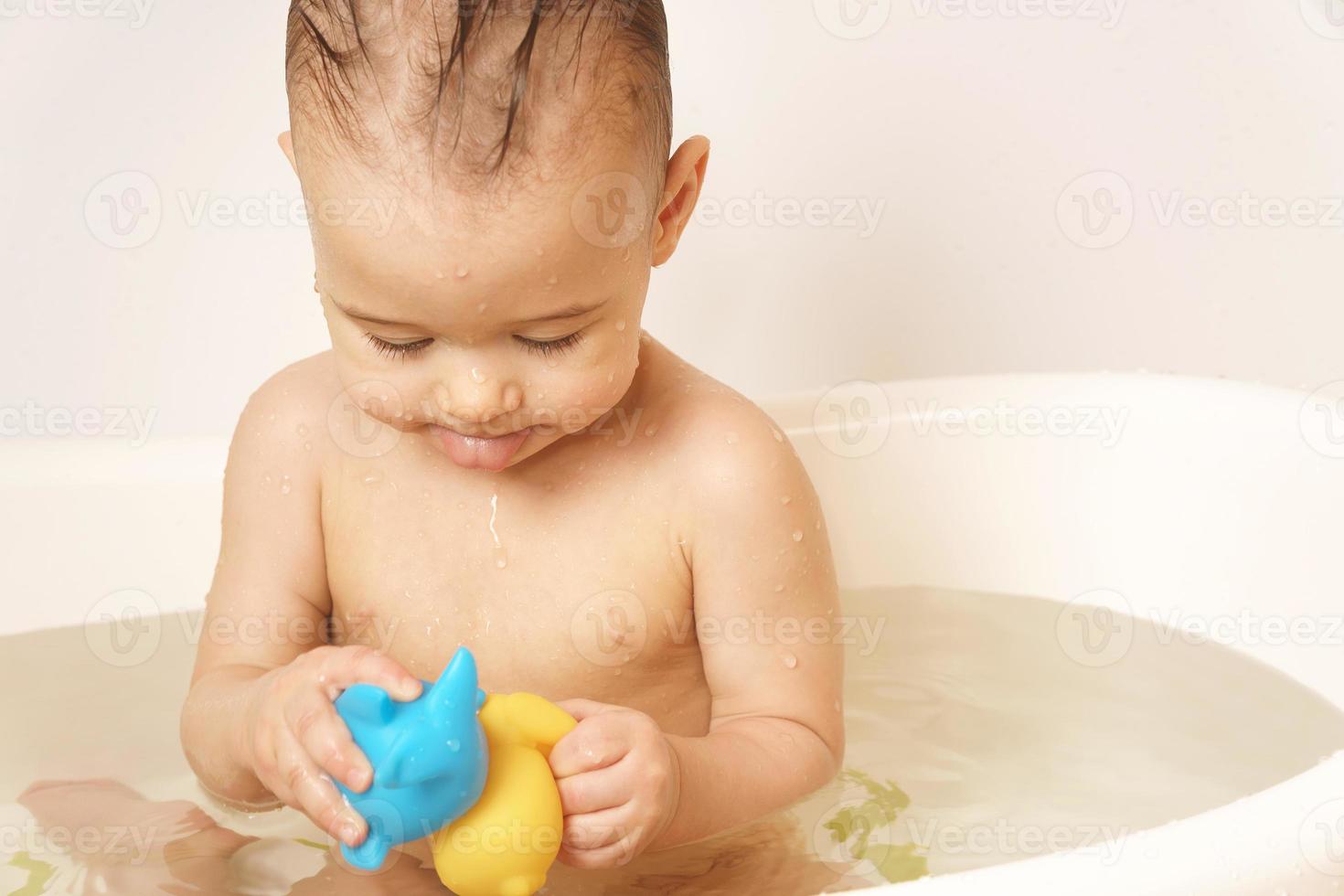 poco ragazzo giocando con gomma da cancellare giocattoli mentre assunzione un' bagno. foto