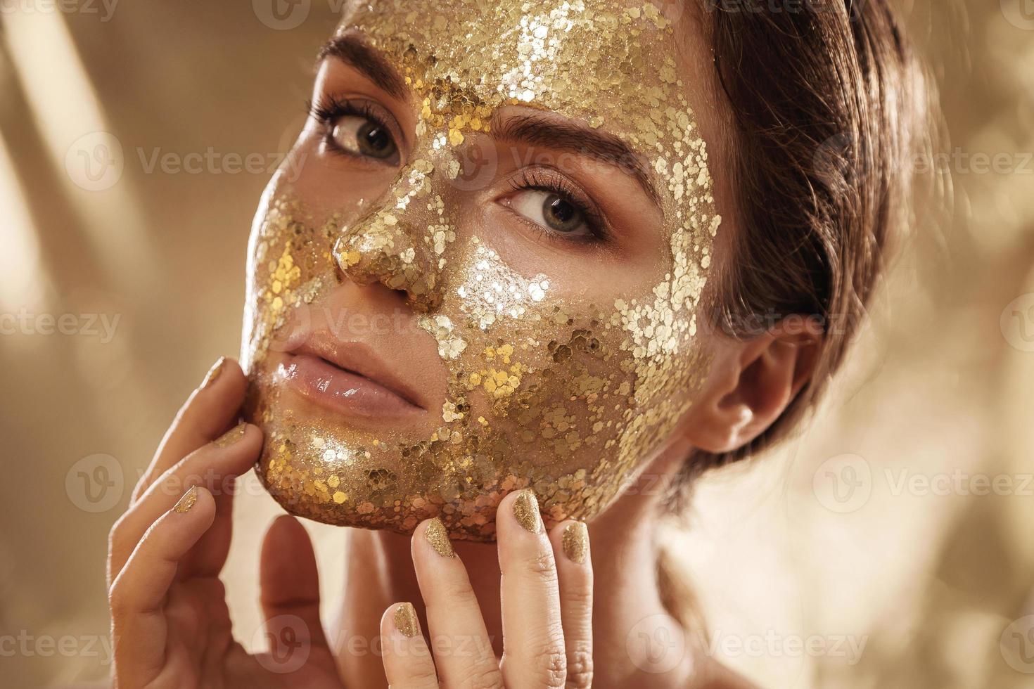 bellissimo donna con d'oro splendente maschera su sua viso per pelle trattamento foto