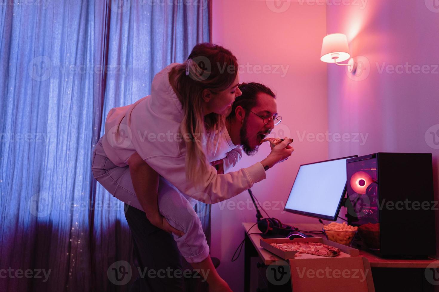 coppia chilling a casa nel camera con neon leggero e mangiare Pizza, Guardando film in linea o giocando video Giochi foto