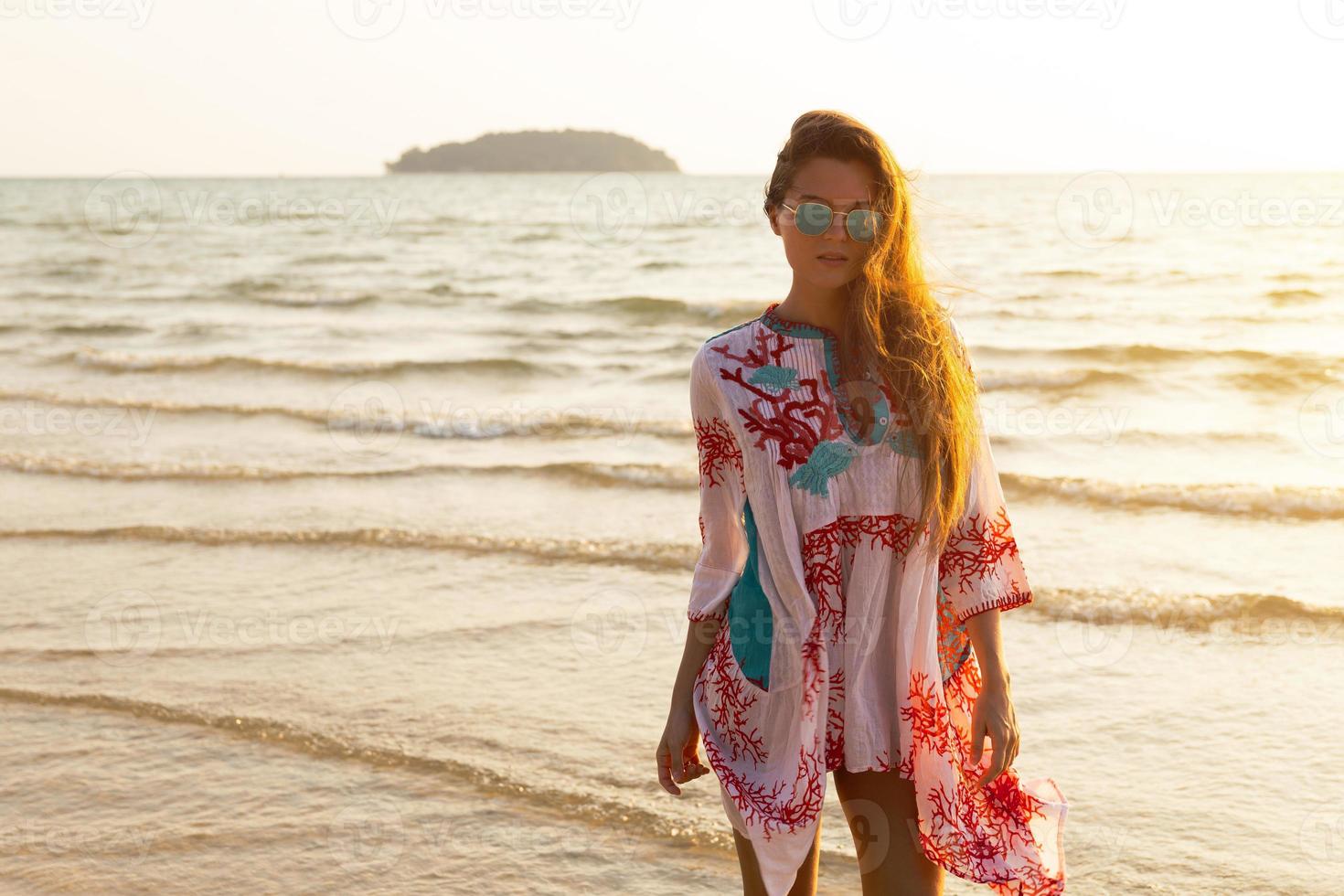 giovane bello donna indossare bellissimo vestito è a piedi di il mare riva foto