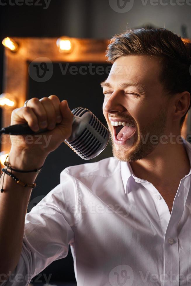 giovane uomo con microfono è cantando a casa foto