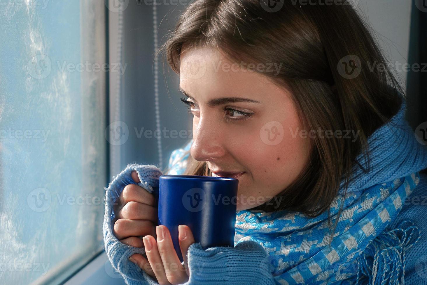 triste bella giovane donna soggiorno casa perché di il influenza e temperatura nel caldo Maglione e sciarpa con tazza di tè vicino il finestra foto