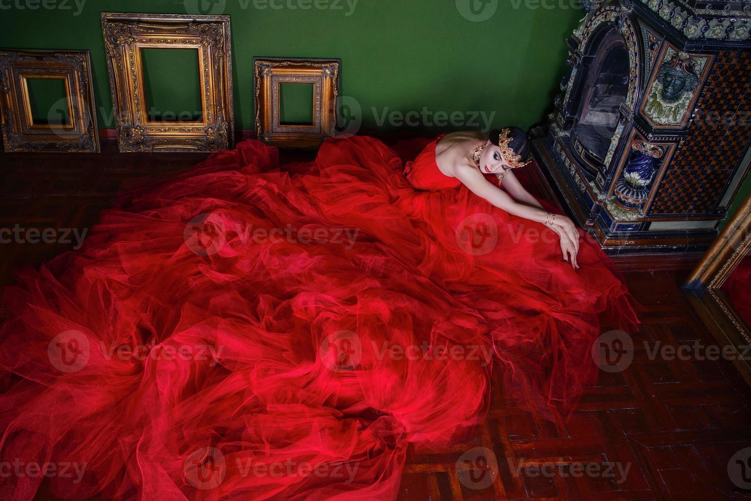 bellissimo donna nel lungo rosso vestito e nel reale corona vicino camino nel lusso interno nel foto studio