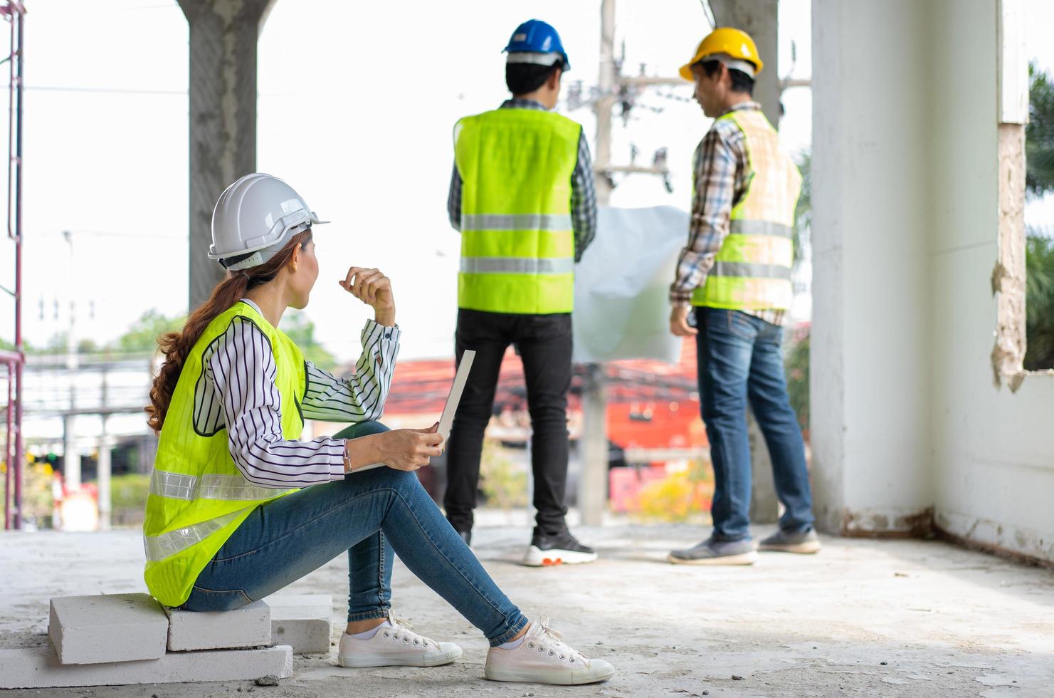 asiatico ingegnere o giovane donna architetto mettere su un' casco per sicurezza e Guarda a planimetria nel il computer portatile per ispezionare edificio fabbrica costruzione luogo e uso parlare con un' contraente foto