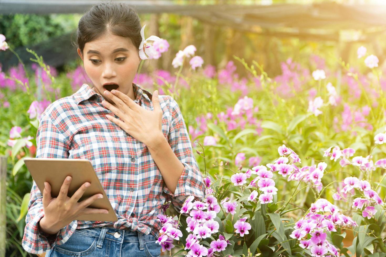 femmina giardinieri indossare plaid camicie. Là erano orchidee raccolta su il orecchie, sua era sorpreso quando Guardando tavoletta e sorridente con la gioia. nuovo generazione contadino, giardinieri concetto. foto