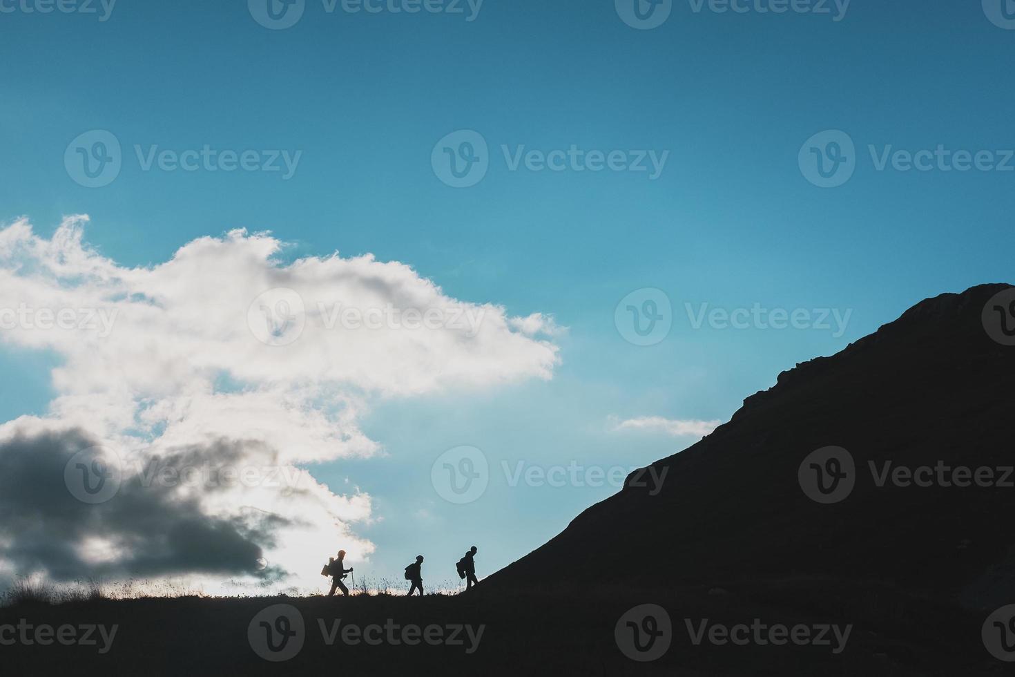 sagome di viaggiatori-turisti arrampicata salita contro il sfondo di nuvole e blu cielo foto