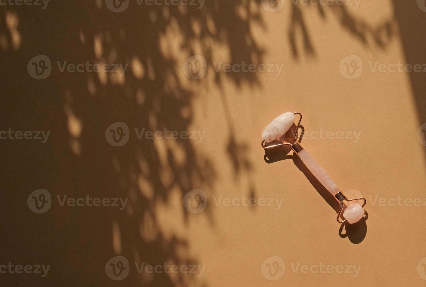 facciale rosa quarzo massaggio rullo o gua sha su beige sfondo con grigio ombra di il le foglie. anti età e sollevamento a casa, facciale massaggio terapia e rilassamento concetto. alternativa medicinale. foto