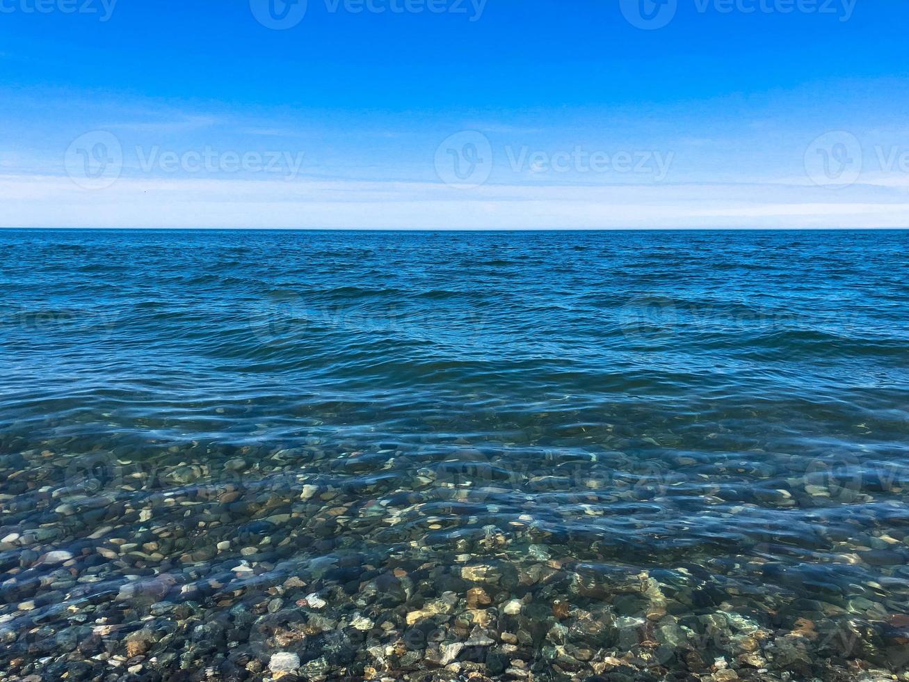 bellissimo multicolore il giro pietre su il mare, fiumi, laghi, stagno, oceano e bollente acqua con onde su il roccioso spiaggia di un' tropicale caldo ricorrere su il orizzonte e cielo. verticale Visualizza foto