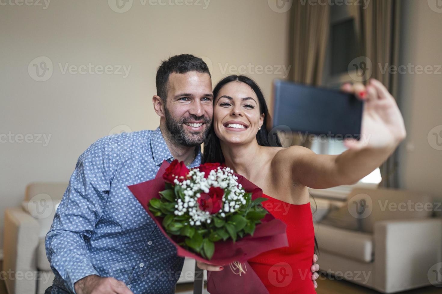 Immagine di contento giovane coppia assunzione autoscatto foto con fiori mentre avendo un' romantico tempo a casa. bello coppia festeggiare San Valentino giorno