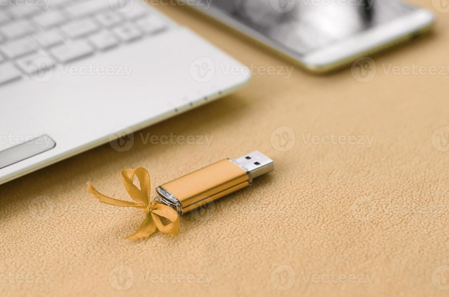 arancia USB veloce memoria carta con un' blu arco bugie su un' coperta di morbido e peloso leggero arancia vello tessuto accanto per un' bianca il computer portatile e smartphone. classico femmina regalo design per un' memoria carta foto